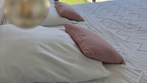 Un dormitorio con un ventanal grande, una cama con almohadas blancas y rosas, y una lámpara colgante.