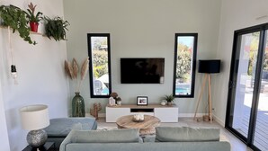 Una sala moderna con un sofá gris, una mesa de centro, un televisor y un ventanal con vistas al exterior.