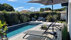 Una terraza de madera con piscina, sillas de descanso y un espacio de estar cubierto.