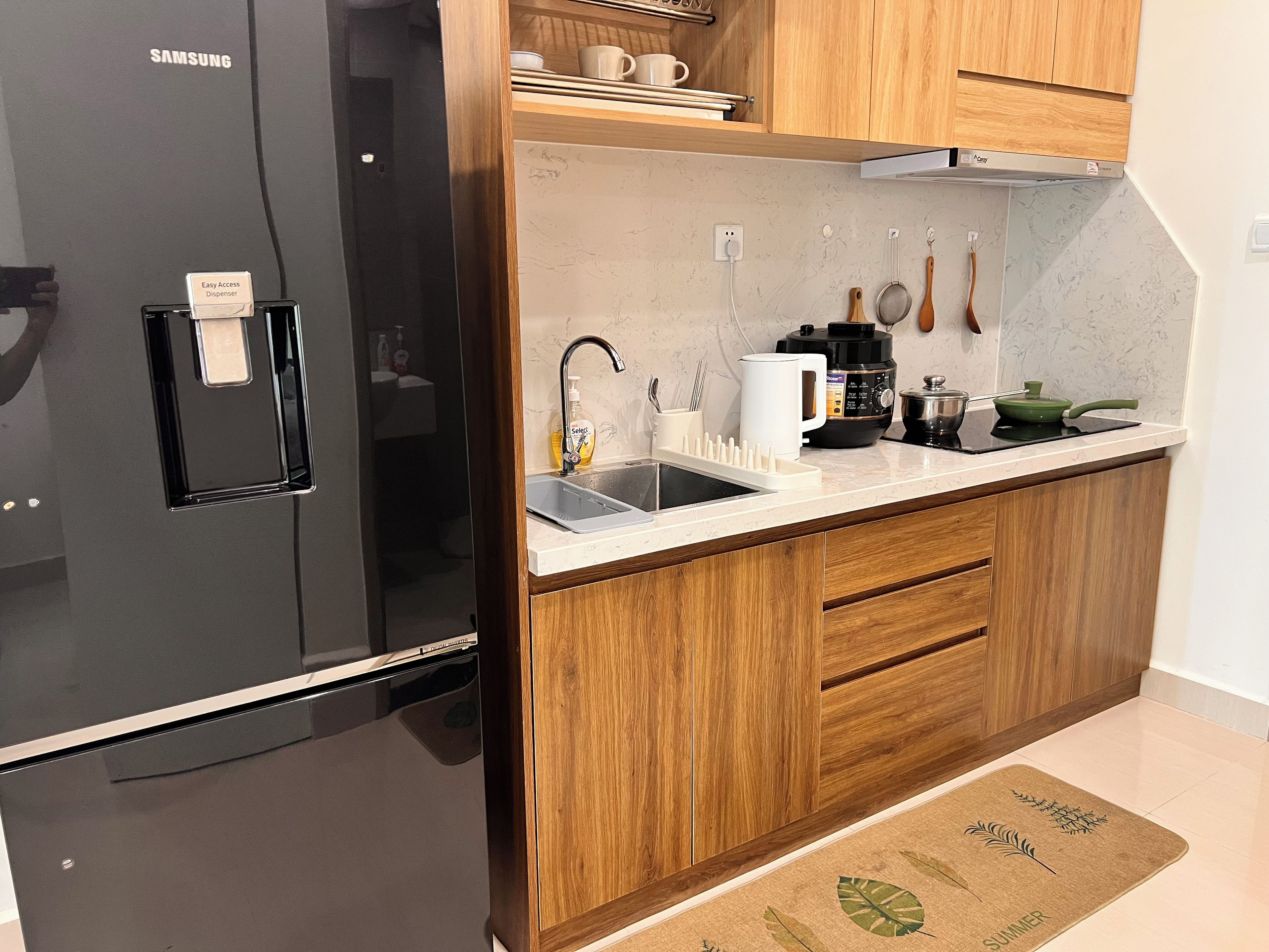 Una cocina moderna con un refrigerador negro, armarios de madera, una encimera blanca y un lavamanos.