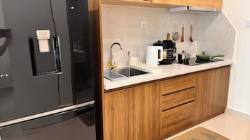 Una cocina moderna con un refrigerador negro, armarios de madera, una encimera blanca y un lavamanos.