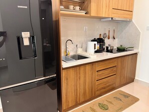 A modern kitchen with a black refrigerator, wooden cabinets, a white countertop, and a sink.