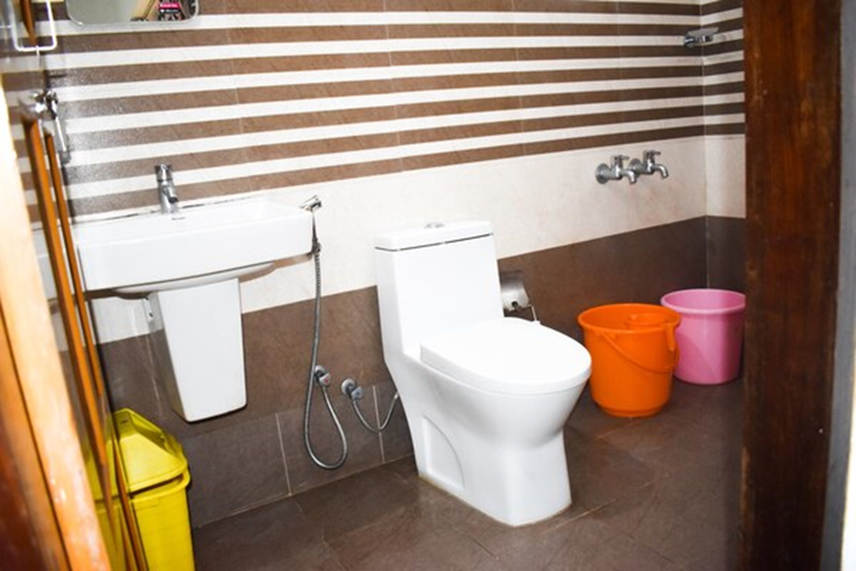 A bathroom with a striped tile wall, a white toilet, a sink, and two buckets.