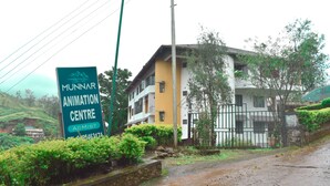 A sign for the Munnar Animation Centre with a view of a yellow building and lush greenery. - AC MIST (Devikolam)