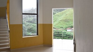 A room with a large window offering a view of a green hillside. - AC MIST (Devikolam)