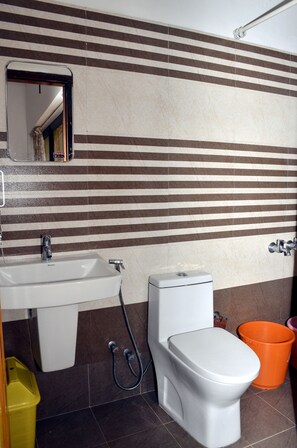 A bathroom with a white sink, a toilet, and a shower. There is a mirror above the sink and a trash bin to the left. - AC MIST (Devikolam)