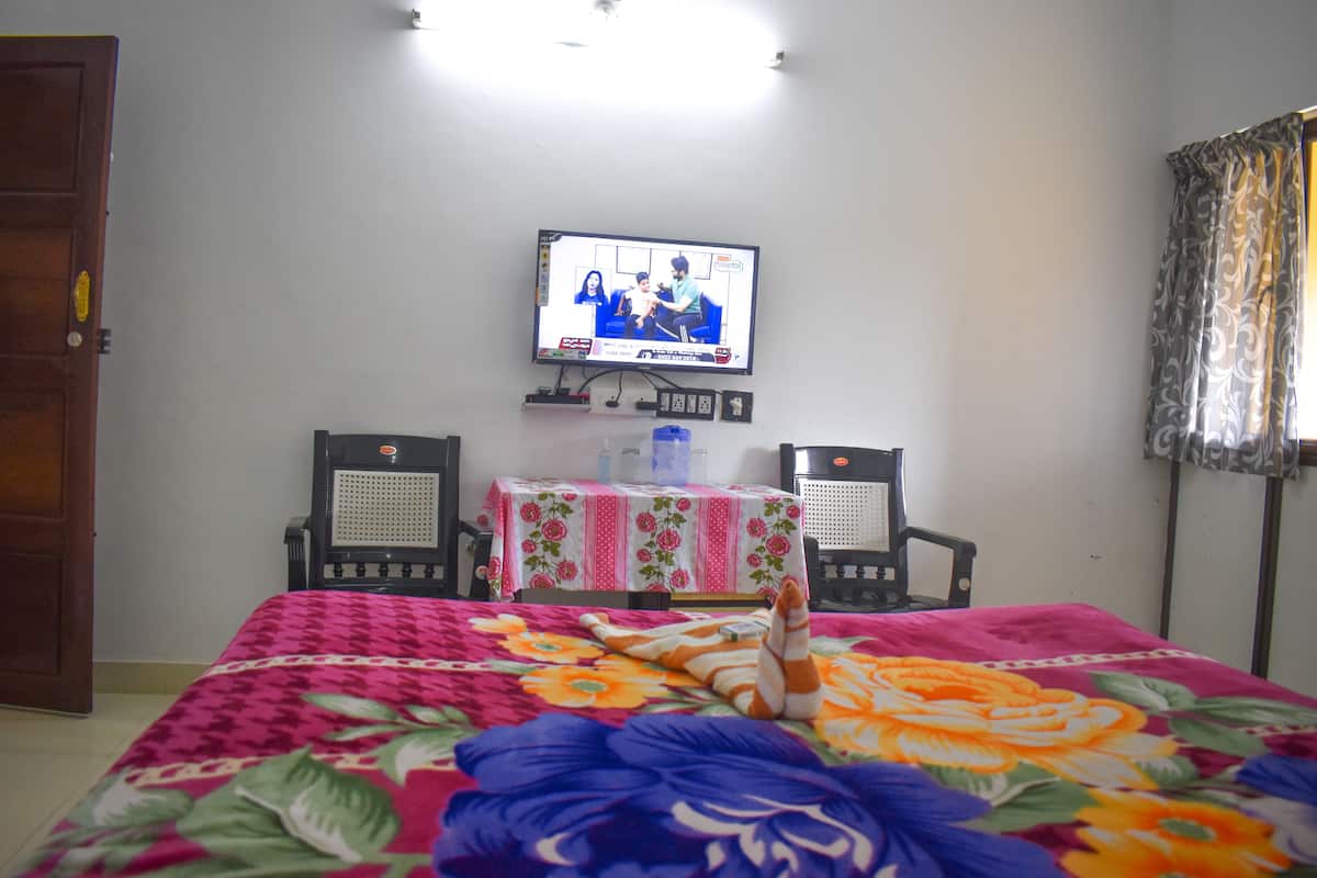 Habitación de hotel con cama, televisor montado en la pared, dos sillas y una mesa con mantel floreado.