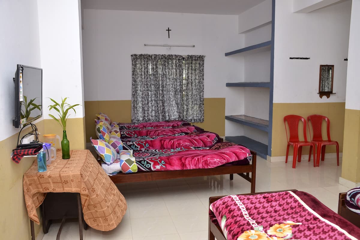 Un dormitorio con cama, escritorio, dos sillas, espejo y una cruz en la pared.