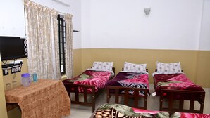 A room with three single beds, a TV, a table with a tablecloth, and a window with curtains. - AC MIST (Devikolam)