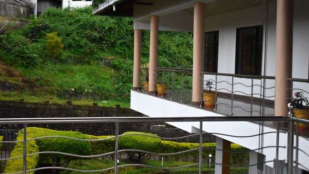 A multi-level building with a balcony, surrounded by lush greenery and a stone wall. - AC MIST (Devikolam)