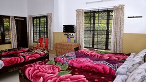 A room with two beds, each with floral bedding, a small table with a mirror, and windows with curtains. - AC MIST (Devikolam)