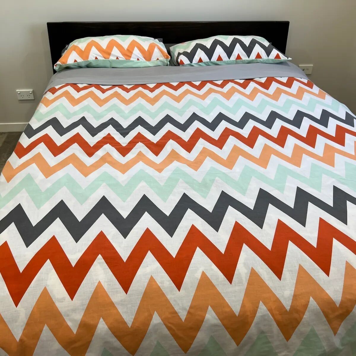 A bed with a multicolored zigzag patterned bedspread and pillows.