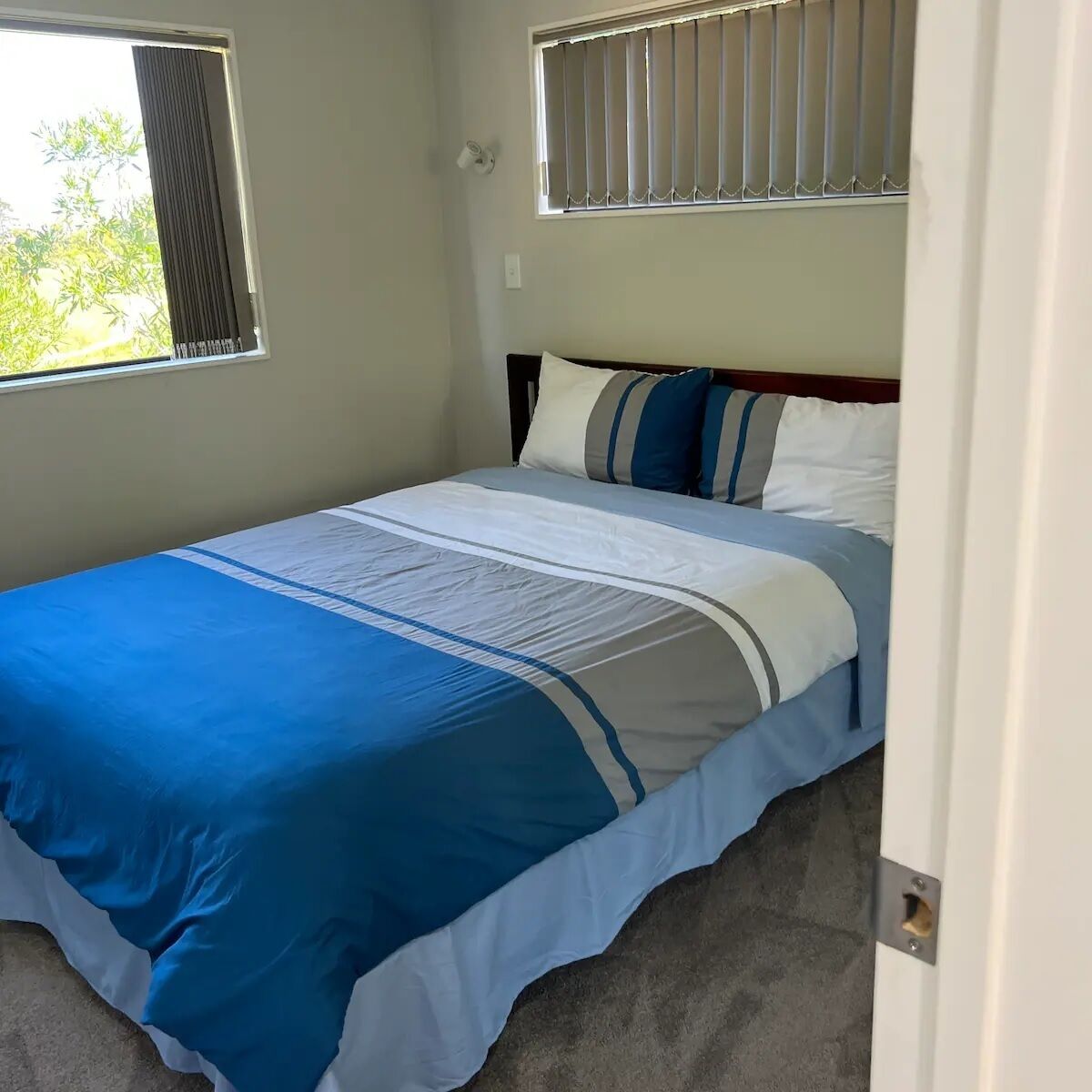 Ein Schlafzimmer mit Bett, Fenster mit Jalousien und einer Tür.