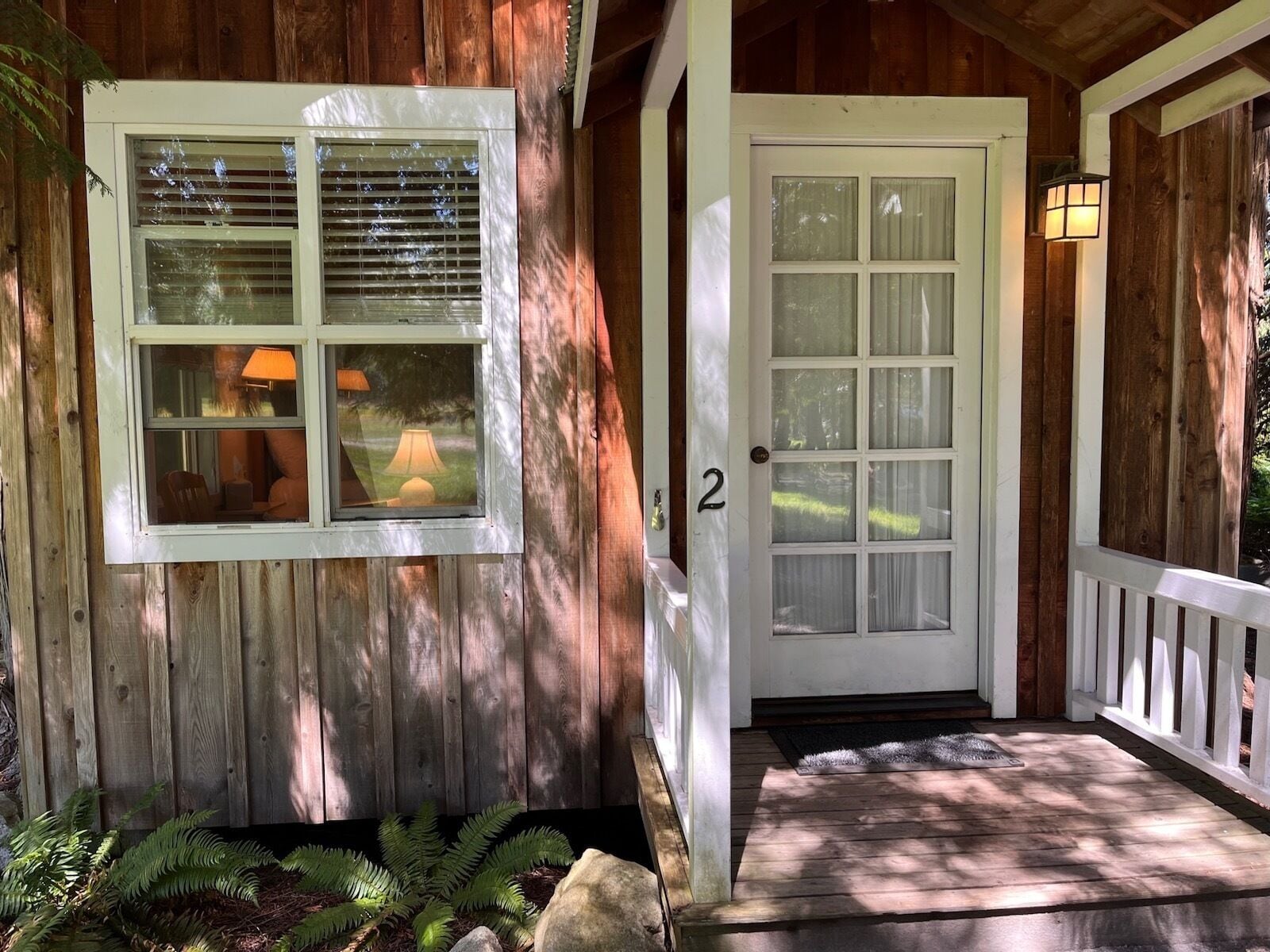 A wooden house with a porch, a front door, and a window with blinds.