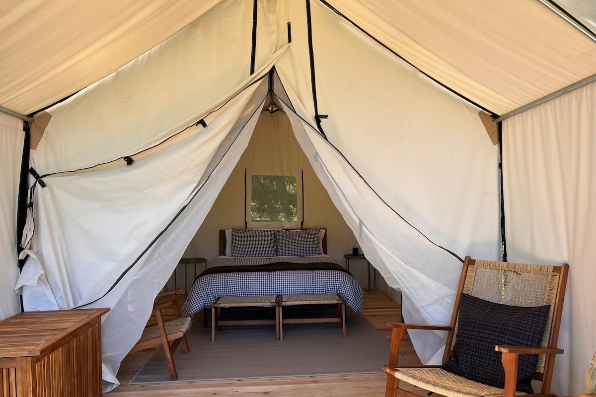 A tent with a bed, two chairs, and a small table.
