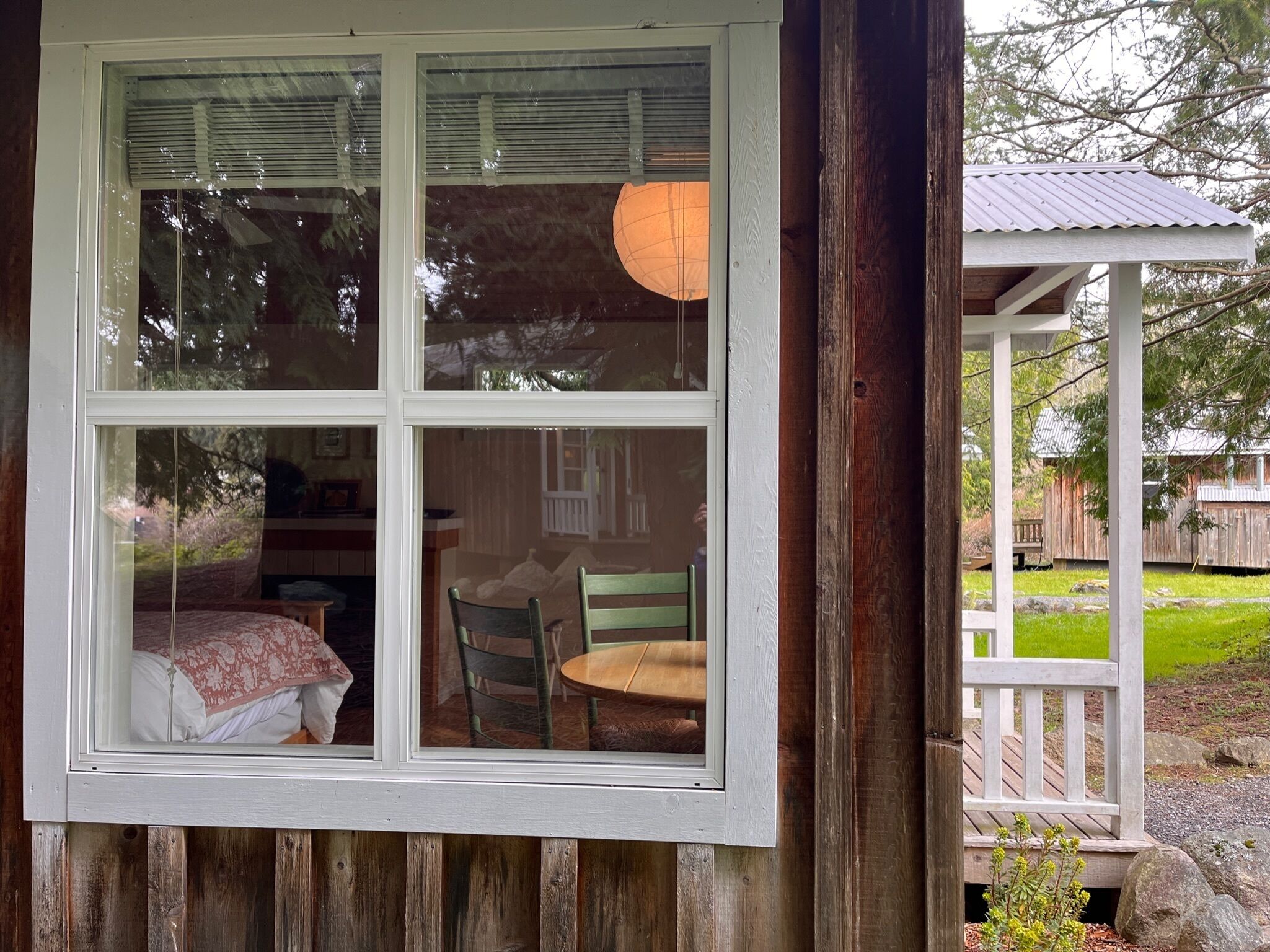 A room with a bed, a chair, and a window overlooking a deck and outdoor area.