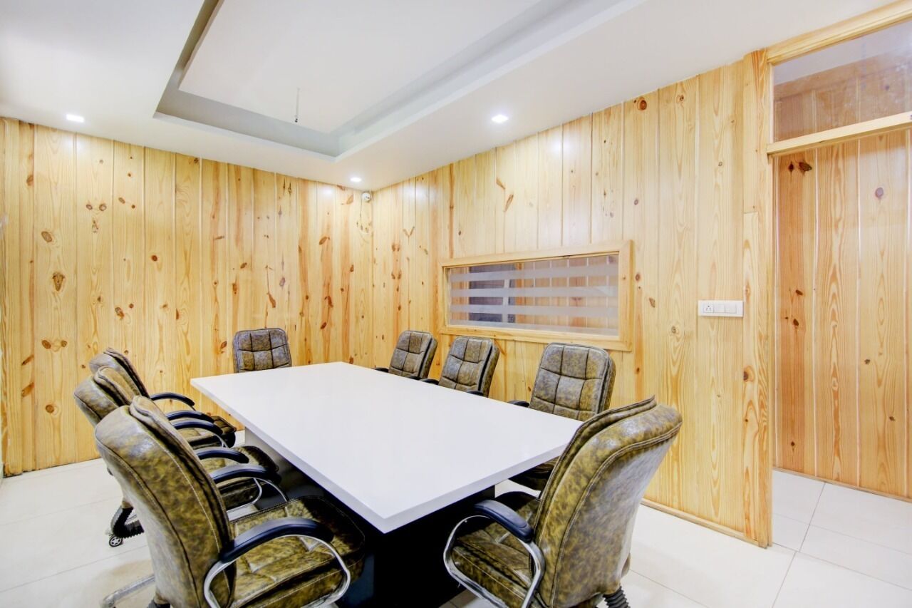 Un salón de conferencias con una mesa grande y seis sillas, paredes de paneles de madera y una ventana con persianas.