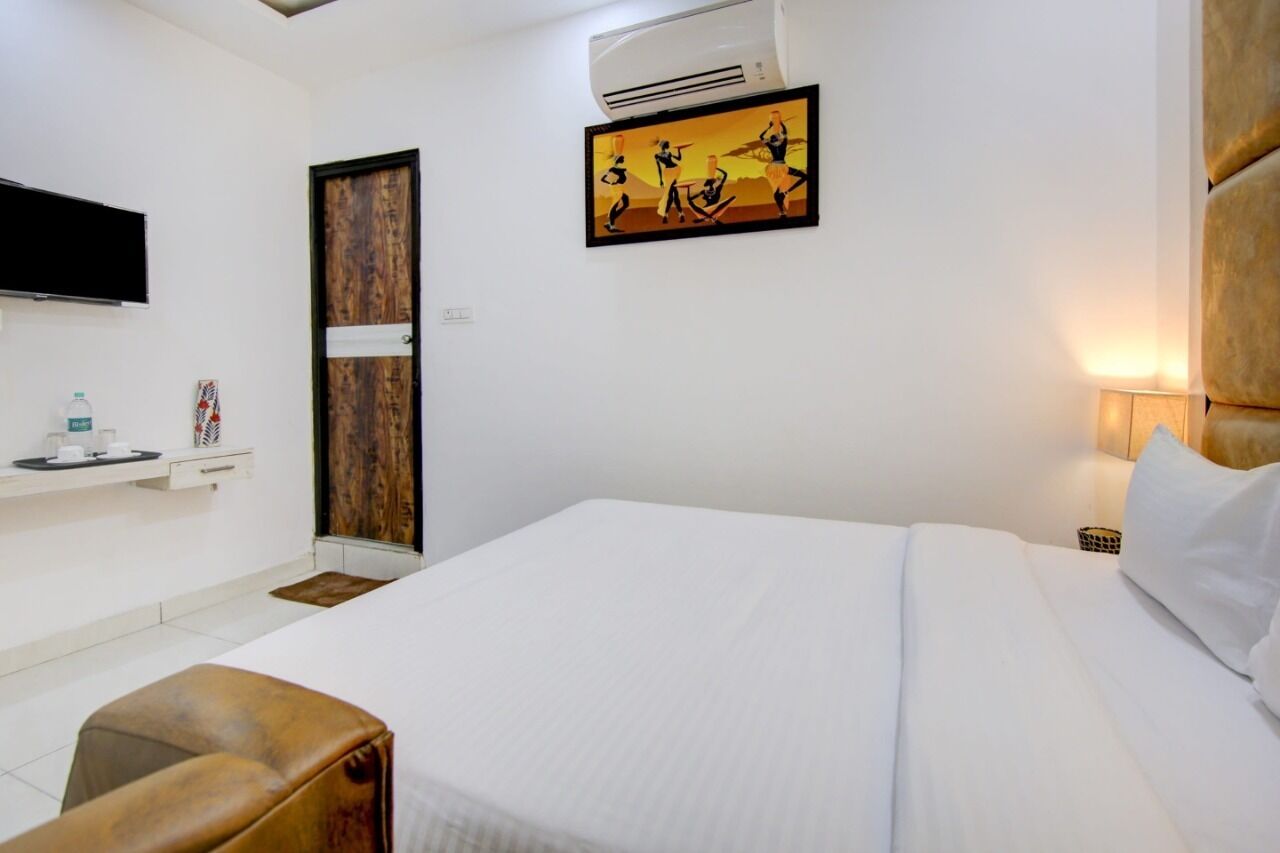 A hotel room with a bed, a desk, a chair, an air conditioner, a TV, and a painting on the wall.