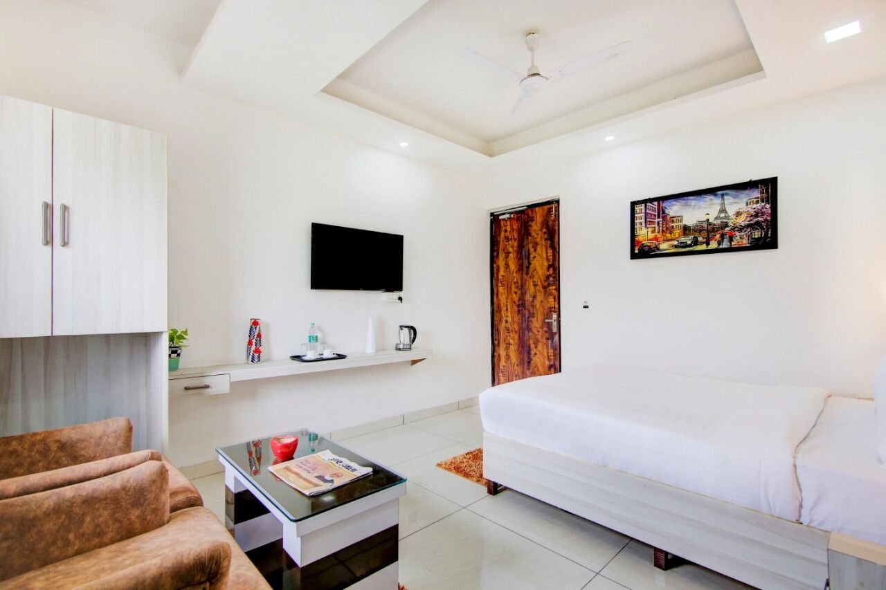 Habitación de hotel moderna con una cama blanca, un televisor de pantalla plana, una puerta de madera y un cuadro de un paisaje urbano.