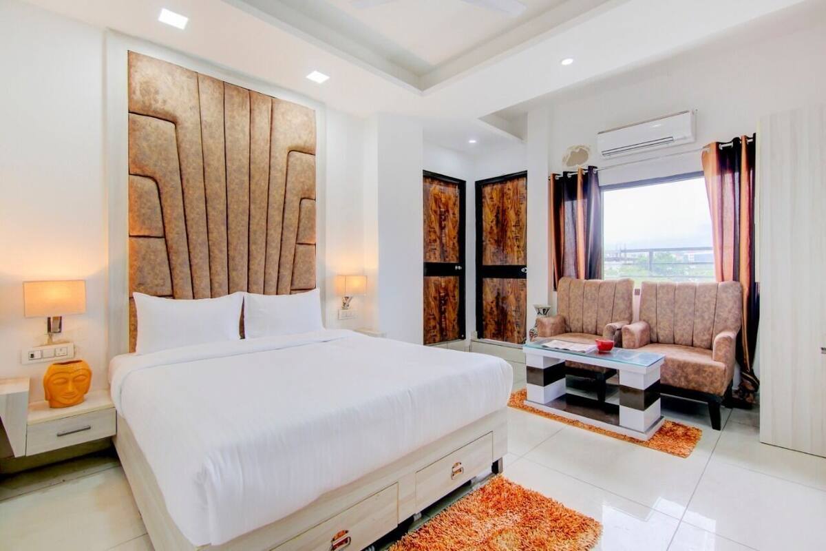 A modern hotel room with a large bed, a sofa, a glass coffee table, and artwork on the walls.