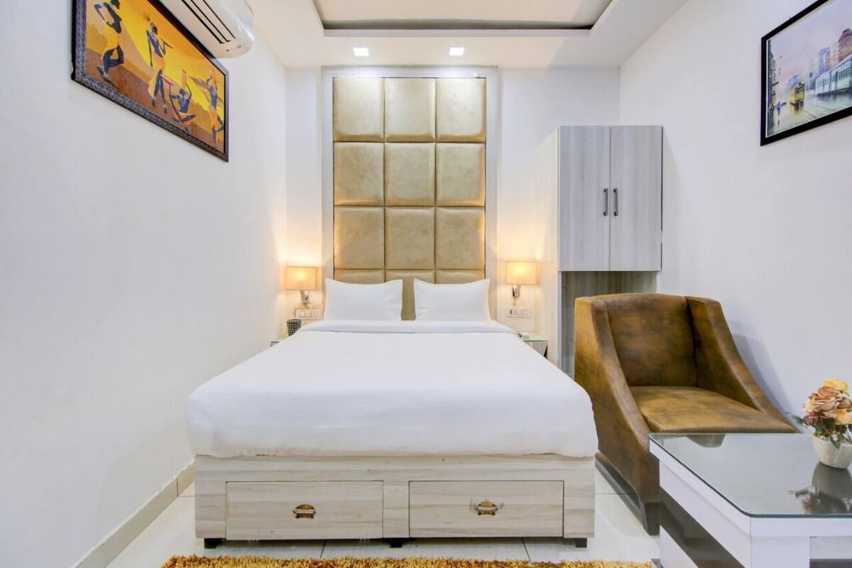 A bedroom with a bed, bedside lamps, a chair, a table, and a wall-mounted air conditioner.