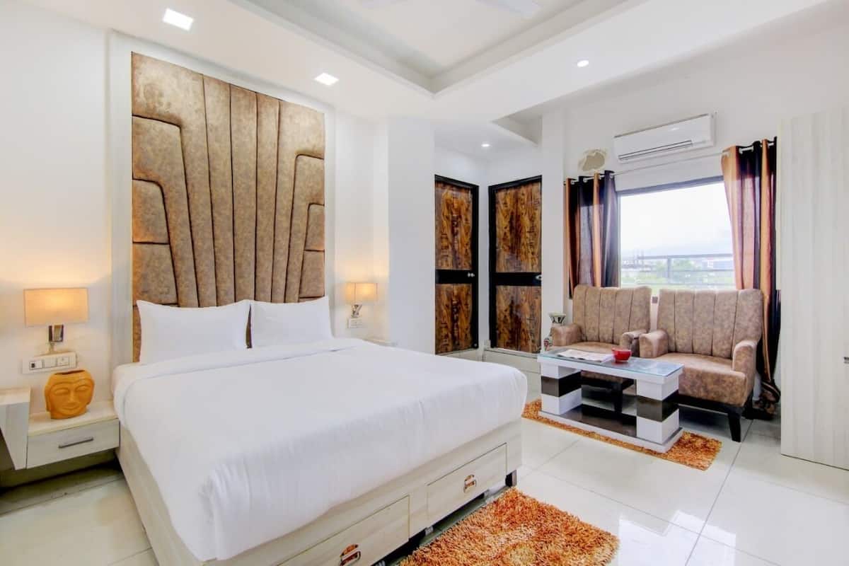 A modern hotel room with a large bed, a sofa, a coffee table, and a view of the city.