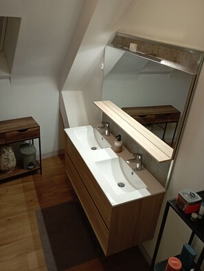 Uma casa de banho moderna com toucador de madeira, um espelho grande e lavatório embutido.