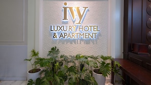 Schild für 'Ivy Luxury Hotel & Apartment' mit geometrischem Wanddesign und Topfpflanzen im Vordergrund.