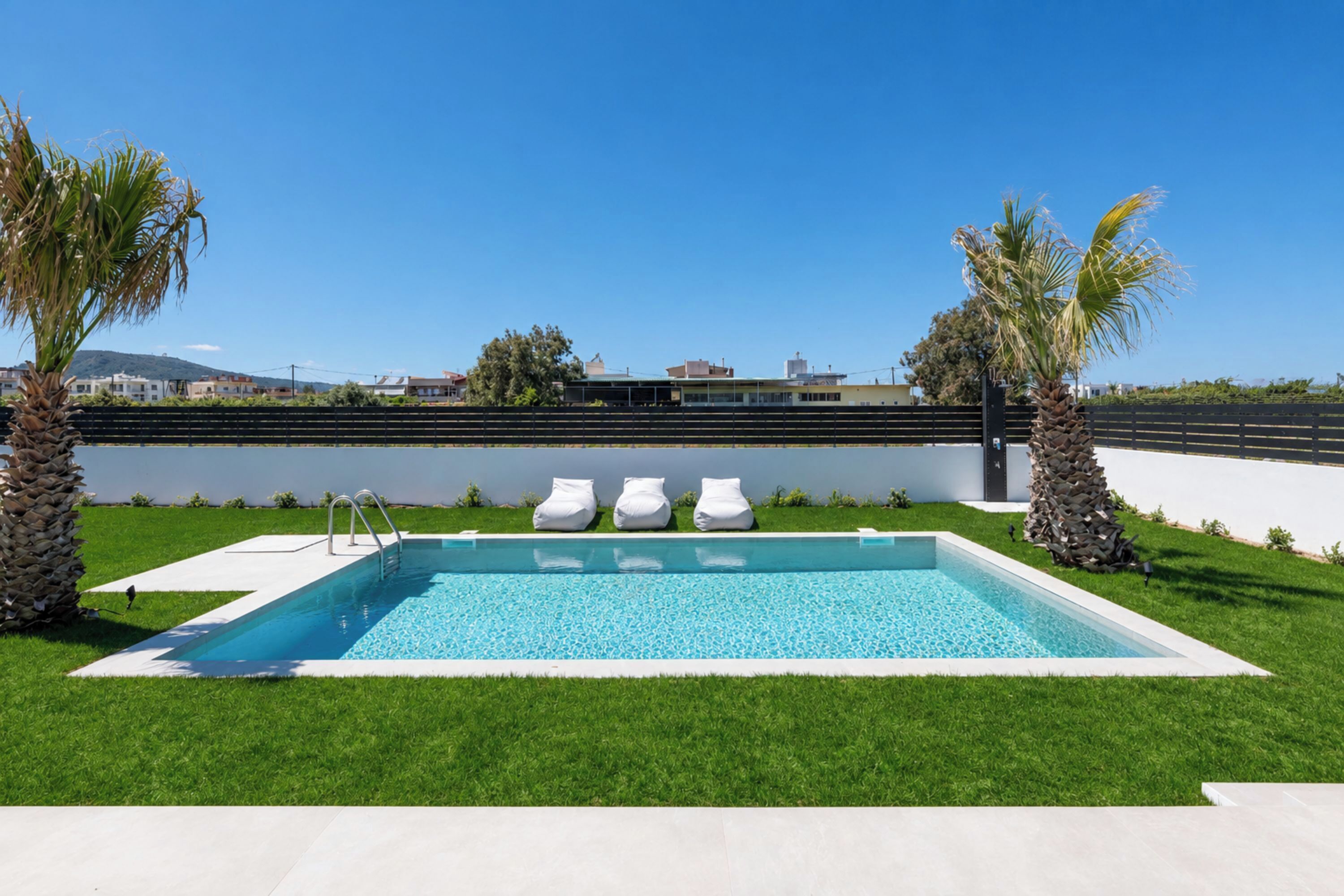 A rectangular swimming pool with a clear blue water surface, surrounded by a well-maintained lawn and two palm trees.