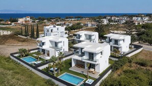 Ein moderner Wohnkomplex mit mehreren zweigeschossigen Häusern, einem Schwimmbad und Blick auf das Meer.