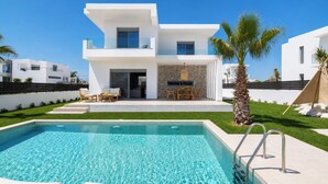 Una casa moderna de dos pisos con piscina, mobiliario exterior y una palmera.