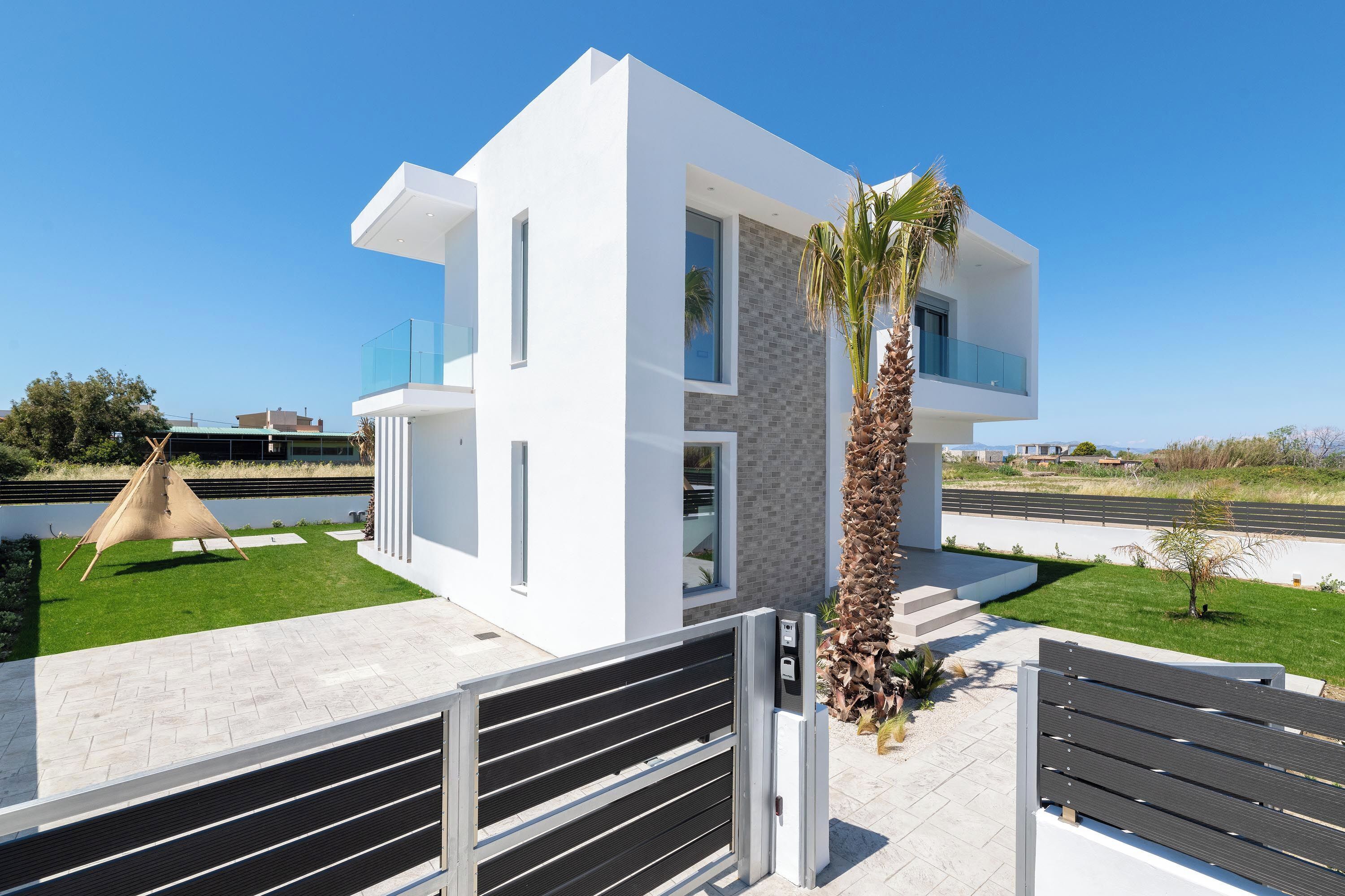 A modern two-story house with a flat roof, large windows, and a balcony.