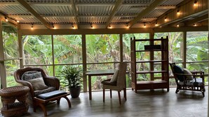 A room with large windows, wicker furniture, and a wooden ceiling.