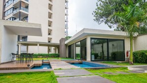 A modern outdoor pool area with a patio, seating, and a building with large windows and a covered walkway. - NAIRO STUDIOS (Nairobi)