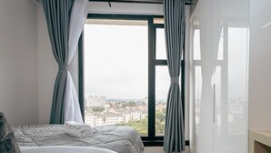 A bedroom with two beds, a view of buildings through a large window, and a wooden floor. - NAIRO STUDIOS (Nairobi)