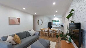A modern living room with a sofa, ottoman, dining table, chairs, and a TV mounted on the wall. - Cozy Newtown 2 bedroom unit (Newtown)