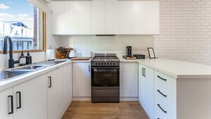 A modern kitchen with white cabinets, a stainless steel stove, and a window overlooking a brick building. - Cozy Newtown 2 bedroom unit (Newtown)