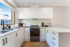 A modern kitchen with white cabinets, a stainless steel stove, and a window overlooking a brick building. - Cozy Newtown 2 bedroom unit (Newtown)