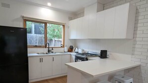 A modern kitchen with white cabinetry, a black refrigerator, a window, and a wooden floor. - Cozy Newtown 2 bedroom unit (Newtown)