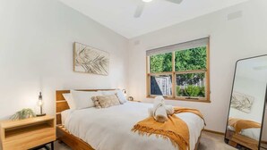 A bedroom with a bed, bedside table, lamp, window, and mirror. - Cozy Newtown 2 bedroom unit (Newtown)