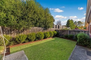 A backyard with a wooden fence, a lawn, and a garden bed. - Cozy Newtown 2 bedroom unit (Newtown)