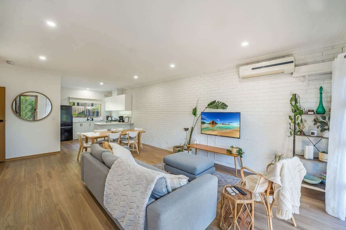 A modern living room with a sofa, a dining area, and a kitchen in the background.