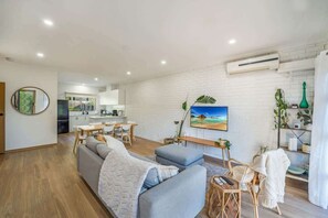 A modern living room with a sofa, a dining area, and a kitchen in the background. - Cozy Newtown 2 bedroom unit (Newtown)