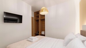 A hotel room with a bed, a TV mounted on the wall, a wardrobe, and a hanging light fixture. - Martini Villas - Rosemary in Kremasti (Κρεμαστή)