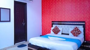 A hotel room with a bed, a red patterned wall, a white headboard, and a black door. - Roomshala 051 Ashok Palace (New Delhi)