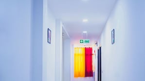 A hallway with white walls, a fire exit sign, and a door with red curtains. - Roomshala 051 Ashok Palace (New Delhi)