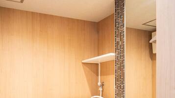 A compact hotel bathroom with a washing machine, a sink, and a mirror.