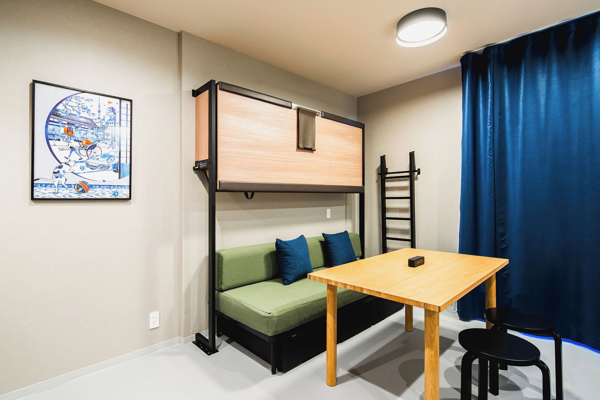 A compact room with a bunk bed, a green sofa with blue cushions, a wooden table, and a black chair.