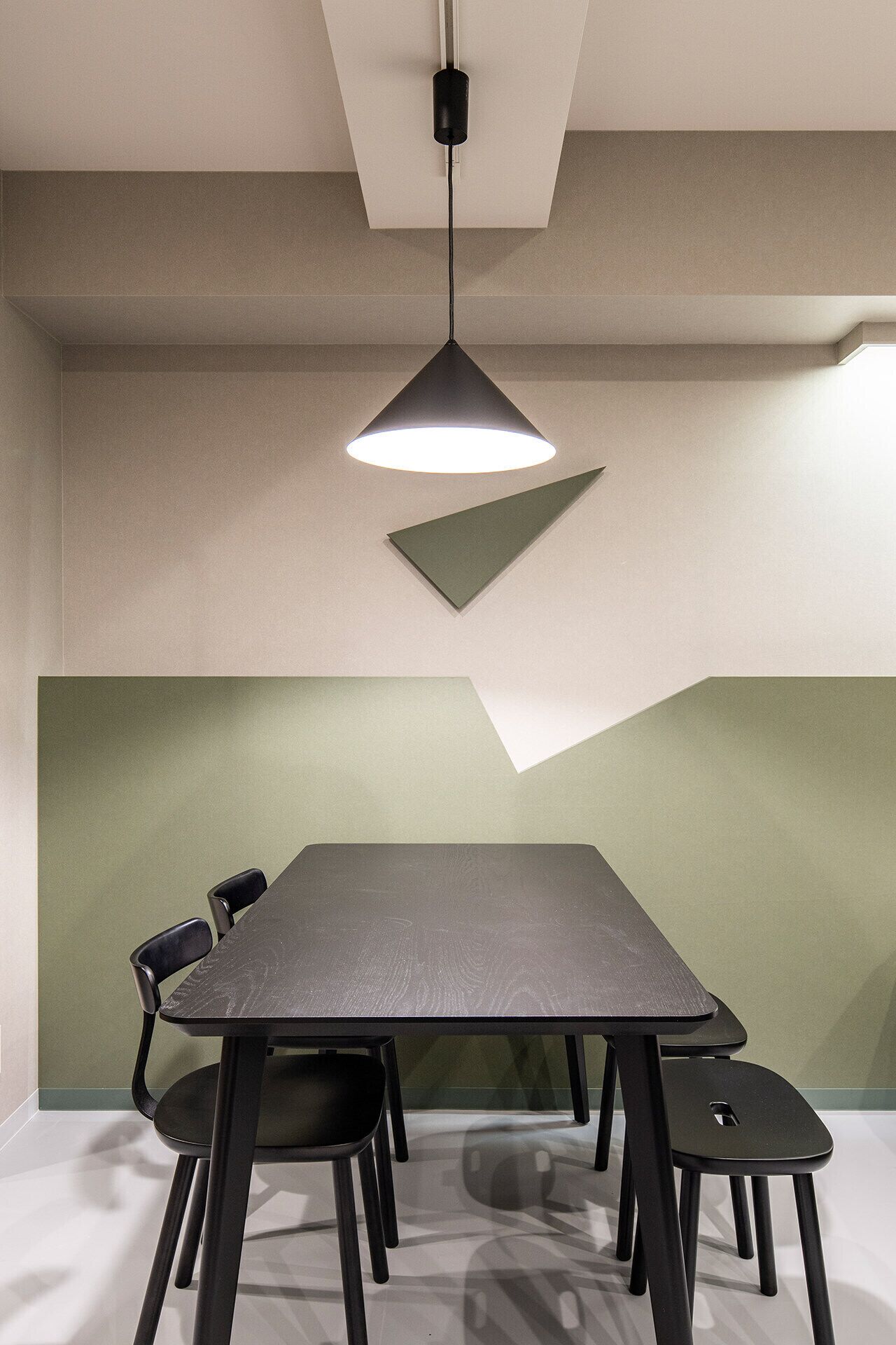 A conference room with a long table, four chairs, a hanging light fixture, and a geometric wall design.