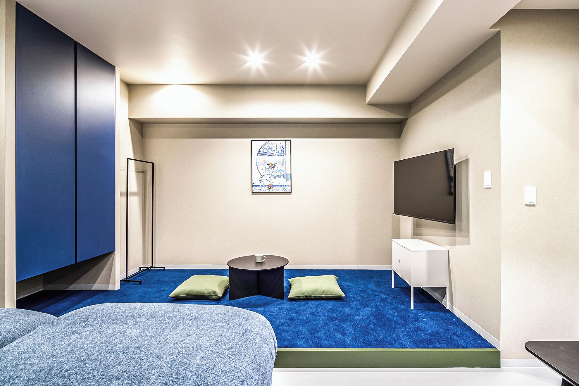 A compact hotel room with a bed, a TV, a small table, and a blue carpet.